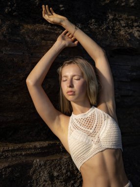 Beyaz bluz giyen çekici beyaz kadın portresi. Sahildeki kayanın yanında duran seksi kadın. Bronzlaşmış deri. Yaz kavramı. Tropikal adaya git. Endonezya, Bali Plajı