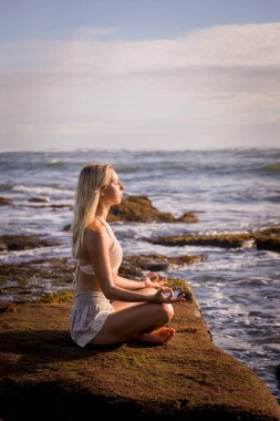 Kumsalda yoga yapan bir kadın. Padmasana 'da oturuyor, Lotus Poz. Eller Gyan Mudra 'da. Pozitif enerji. Sağlıklı yaşam konsepti. Yoga inzivası. Uzayı kopyala Okyanus manzaralı. Endonezya, Bali Plajı