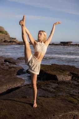 Yoga pratiği. Beyaz kadın Samsahate Hanumanasana, Standing Split Poose 'da çalışıyor. Bacak kasları geriliyor. Denge ve konsantrasyon. Yoga inzivası. Okyanus manzaralı. Endonezya, Bali Plajı