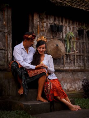 Mutlu, çok kültürlü bir çift. Romantik bir kavram. Birbirine aşık bir çift. Bambu evi. Beyaz kadın ve Balili koca geleneksel kıyafetler giyiyor. Penglipuran köyü, Bali, Endonezya