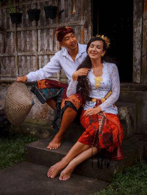 Mutlu, çok kültürlü bir çift. Romantik bir kavram. Birbirine aşık bir çift. Bambu evi. Beyaz kadın ve Balili koca geleneksel kıyafetler giyiyor. Şapkalı adam. Penglipuran köyü, Bali, Endonezya
