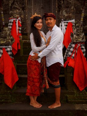 Bali 'deki tapınağın yanında duran çok kültürlü bir çift. Beyaz kadın ve Balili koca geleneksel kıyafetler giyiyor. Kültür ve din. Penglipuran köyü, Bali, Endonezya