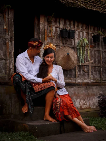 Mutlu, çok kültürlü bir çift. Romantik bir kavram. Birbirine aşık bir çift. Bambu evi. Beyaz kadın ve Balili koca geleneksel kıyafetler giyiyor. Penglipuran köyü, Bali, Endonezya