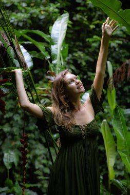 Yeşil elbiseli, tropik yağmur ormanlarında yürüyen güzel bir kadın. Ormandaki kadın büyük yaprağa dokunuyor ve gülümsüyor. Doğa ve çevre kavramı. Asya 'ya git. Bali Adası, Endonezya