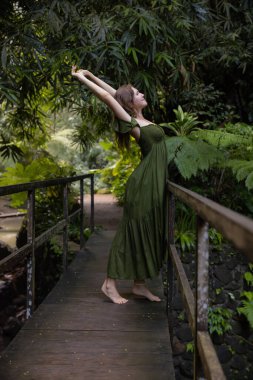 Tropikal ormanda köprüde gerinen güzel bir kadın. Yeşil elbise giyen beyaz bir kadın. Doğa ve çevre kavramı. Asya 'ya git. Bali Adası, Endonezya