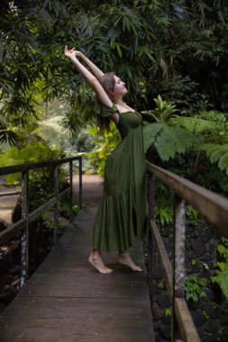 Tropikal yağmur ormanlarında köprüde gerinen güzel bir kadın. Yeşil elbise giyen beyaz bir kadın. Doğa ve çevre kavramı. Asya 'ya git. Bali Adası, Endonezya