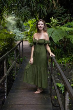 Tropikal yağmur ormanlarında köprüde duran güzel, gülümseyen kadın. Yeşil elbise giyen beyaz bir kadın. Doğa ve çevre kavramı. Asya 'ya git. Bali Adası, Endonezya