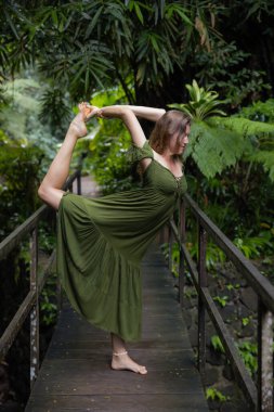 Tropikal ormanda köprüde yoga yapan beyaz bir kadın Natarajasana 'da duruyor, Dans Pozu Lordu. Dengede duruyor, Asana 'yı büküyor. Asya 'ya git. Sağlıklı bir yaşam tarzı. Bali, Endonezya