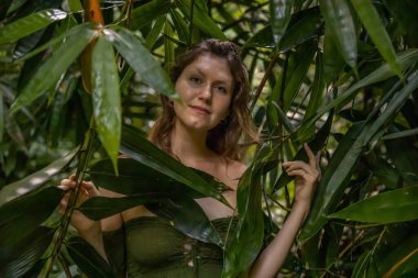 Kadının yüzü bambu yapraklarıyla çevrili. Tropikal yağmur ormanlarında güzel bir kadının portresi. Ormanda yemyeşil bitkiler. Doğa konsepti. Bali Adası, Endonezya