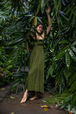 Tropikal yağmur ormanlarında yürüyen, uzun yeşil elbiseli güzel bir kadın. Kapalı gözler. Ormanda bir kadın bambu yapraklarına dokunuyor. Doğa ve çevre kavramı. Asya 'ya git. Bali Adası, Endonezya