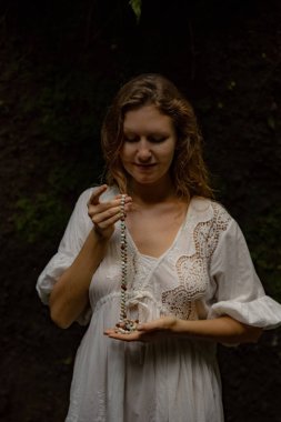 Beyaz kadın dua ve meditasyon için Mala 'yı tutuyor. Budist japa mala doğal taşlardan yapılmış. Din kavramı. Budist mücevherleri. Beyaz elbiseli bir kadın. Bali, Endonezya