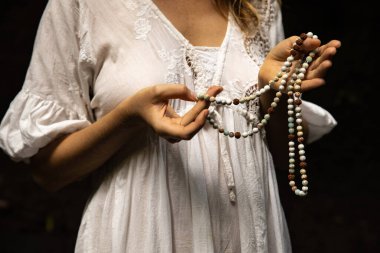 Japon mala 108 boncuğu doğal taşlardan. Kadının eli yakın. Dua ve meditasyon. Budist mücevherleri. Değerli boncuk iplikleri. Din kavramı. Beyaz elbise. Siyah arka plan. Bali, Endonezya