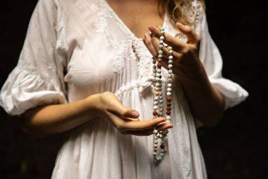 Japon mala 108 boncuğu doğal taşlardan. Kadının elleri kapalı. Dua ve meditasyon. Budist mücevherleri. Değerli boncuk iplikleri. Din kavramı. Beyaz elbise. Siyah arka plan. Bali Endonezya