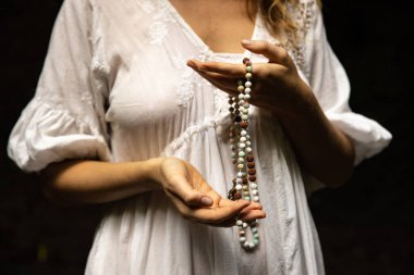 Japon mala 108 boncuğu doğal taşlardan. Kadının elleri kapalı. Dua ve meditasyon. Budist mücevherleri. Değerli boncuk iplikleri. Din kavramı. Beyaz elbise. Siyah arka plan. Bali Endonezya
