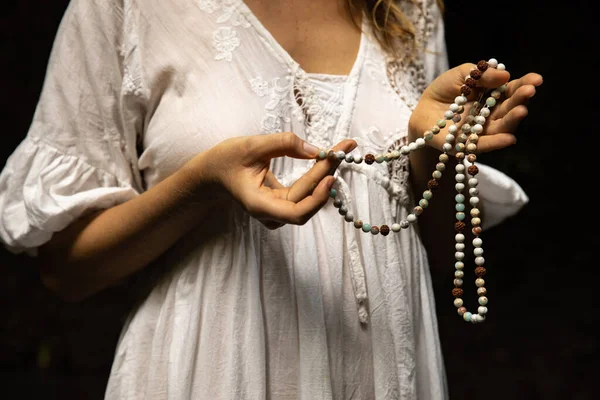 Japon mala 108 boncuğu doğal taşlardan. Kadının elleri kapalı. Dua ve meditasyon. Budist mücevherleri. Değerli boncuk iplikleri. Din kavramı. Beyaz elbise. Siyah arka plan. Bali Endonezya