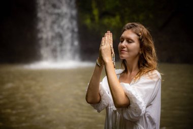 Beyaz kadın dua ve meditasyon için Mala 'yı tutuyor. Budist japa malası. Eller namaste mudra 'da. Din kavramı. Budist mücevherleri. Beyaz elbiseli bir kadın. Tibuman Şelalesi, Bali, Endonezya