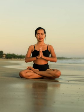 Sahilde yoga antrenmanı. Lotus pozu. Padmasana. Eller namaste mudra 'da. Kapalı gözler. Meditasyon ve konsantrasyon. Zen hayatı. Bedensel ve zihinsel rahatlama. Yoga inzivası. Gün batımı zamanı. Seminyak, Bali