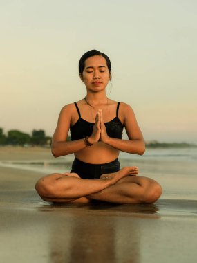 Sahilde yoga antrenmanı. Lotus pozu. Padmasana. Eller namaste mudra 'da. Kapalı gözler. Meditasyon ve konsantrasyon. Zen hayatı. Bedensel ve zihinsel rahatlama. Yoga inzivası. Gün batımı zamanı. Seminyak, Bali