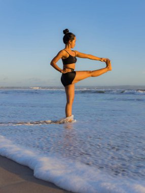 Sahilde yoga antrenmanı. Utthita Hasta Padangusthasana, Uzatılmış Elden Büyük Parmağa Poz. Asana 'yı dengeliyorum. Mükemmel bir vücut. Sağlıklı bir yaşam tarzı. Yoga inzivası. Uzayı kopyala Seminyak plajı, Bali