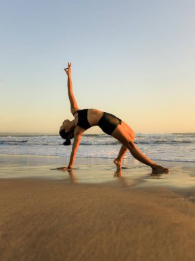 Yoga inzivası. Güzel Asana. İnce kadın sahilde yoga yapıyor. Esneme egzersizi. Esnek vücut. Uzayı kopyala Dikey yerleşim. Seminyak Sahili, Bali, Endonezya