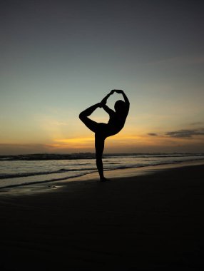Yoga silueti. Sunset plaj yogası. Dans Pozu Lordu, Asana Natarajasana 'da çalışan zayıf bir kadın. Dengede duruyor, Asana 'yı büküyor. Uzayı kopyala Seminyak Sahili, Bali, Endonezya