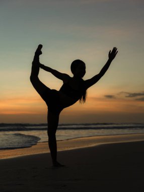 Yoga silueti. Sunset plaj yogası. Dans Pozu Lordu, Asana Natarajasana 'da çalışan zayıf bir kadın. Dengede duruyor, Asana 'yı büküyor. Kumsalda egzersiz. Seminyak Sahili, Bali, Endonezya