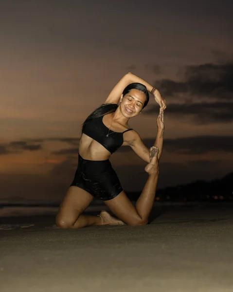 Yoga retreat. Slim Asian woman practicing Eka Pada Rajakapotasana. Mermaid Pose. Pigeon variation. Hip opener, heart-opener, backbend. Fit body. Sunset beach yoga. Seminyak beach, Bali, Indonesia