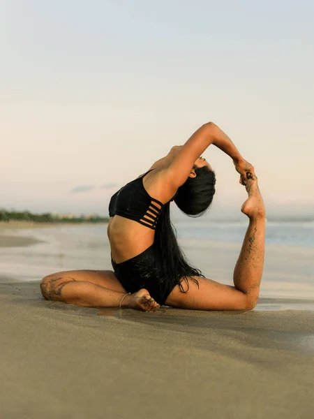 Yoga retreat. Slim woman practicing Eka Pada Rajakapotasana, One Legged King Pigeon Pose. Chest opener improving breathing. Self care concept. Beach retreat. Seminyak beach, Bali, Indonesia