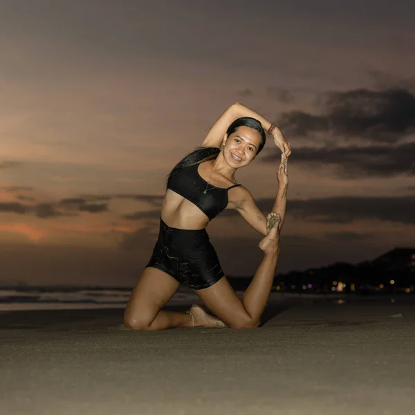 Yoga retreat. Slim Asian woman practicing Eka Pada Rajakapotasana. Mermaid Pose. Pigeon variation. Hip opener, heart-opener, backbend. Fit body. Sunset beach yoga. Seminyak beach, Bali, Indonesia