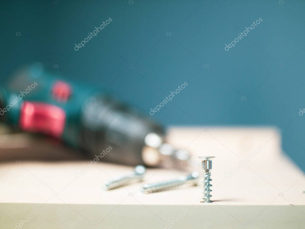 furniture screws and a screwdriver against the background of assembled furniture in the apartment.
