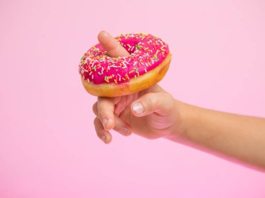 Bir çocuğun parmağına takılmış pembe bir çörek. Yiyeceklerle iyi eğlenceler. Pembe arka planda çilekli tatlı çörek.
