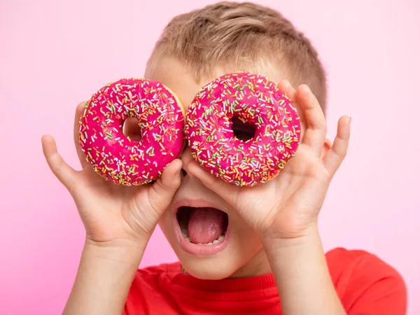 Ergen, donutları karıştırarak eğleniyordu. Bir çocuk pembe arka planda çöreklerle eğleniyor. Yiyeceklerle eğlenceli zaman