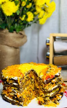 Beyaz tabakta havuçlu ve soğanlı ciğer keki. Yürekli et yemeği. Arka plandaki kavanozlarda baharatlar, masadaki vazoda sarı çiçekler..