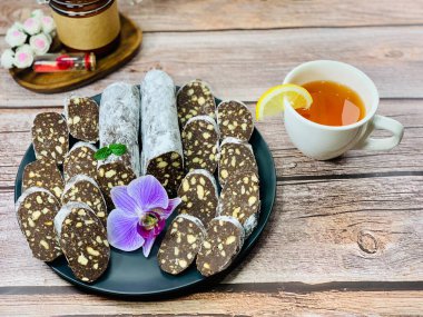 Çikolatalı sosis şeklinde geleneksel tatlı. Siyah tabakta kurabiyeler. Tahta kahverengi arka plan. Yemekle fotoğraf..