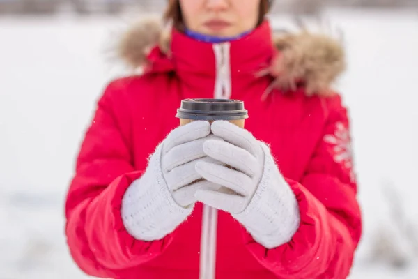 冬天穿着红色夹克的年轻女人拿着一杯热咖啡或茶 一个大雪的冬天 一杯热饮来保暖 冬天喝一杯咖啡 — 图库照片