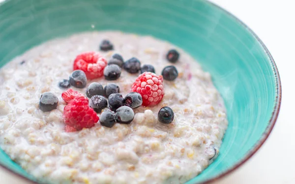Oatmeal porridge in a plate with currant and raspberry berries. — Stock Photo, Image