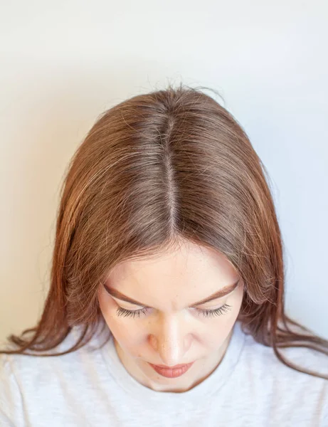A woman\'s head with a parting of gray hair that has grown roots due to quarantine. Brown hair on a woman\'s head close-up.