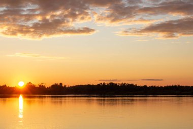 Sakin bir gölde güneşli, renkli bir gün batımı. Güneş suyun yüzeyine yansıyor..