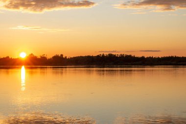 Sakin bir gölde güneşli, renkli bir gün batımı. Güneş suyun yüzeyine yansıyor..