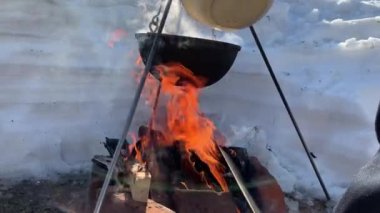 Bir turist tenceresi kışın kamp ateşinin başında durur ve kışın doğada ateş yakar. Adam kazan kapağını açıyor, 4K