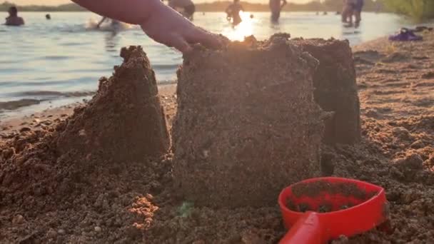 小さな子供が日没時に池の近くのビーチで遊んでいます 砂で家を建て破壊する 休暇中の子供たちとの休暇の概念 — ストック動画