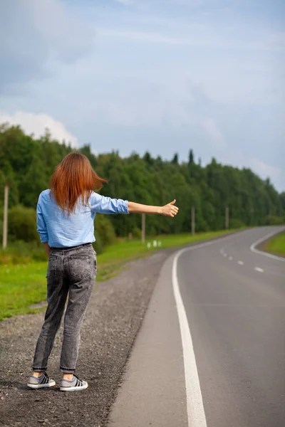 少女は手で高速道路の車を止めます 道路上のスタイリッシュな女性は車の旅に行く停止します 森の中の道 — ストック写真