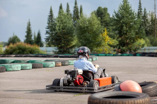 A girl or a woman in a hard hat rides a go-kart on a special track fenced with rubber wheels. Active recreation and sports on transport. Preparation and training for competitions.