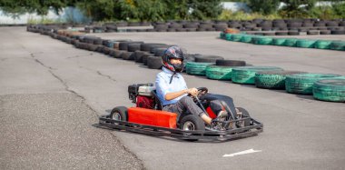 Sert şapkalı bir kız veya kadın özel bir pistte lastik tekerleklerle çevrili bir go-kart kullanıyor. Aktif eğlence ve spor araçları. Yarışmalar için hazırlık ve eğitim. 