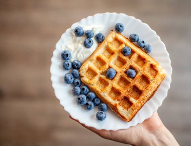 Bir kadın elinde böğürtlenli taze waffle tabağı tutar. Çilek ve yabanmersinli ev yapımı waffle. Meyveli Lezzetli Kahvaltı.