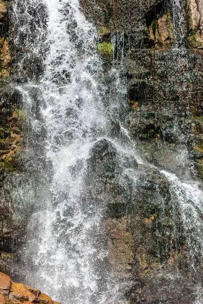 Yüksek kalitede güçlü bir şelaleye yakın çekim. Vahşi doğada güneşten sırılsıklam olmuş bir şelalenin yan görüntüsü. Dağdan büyük bir su akıntısı akıyor..