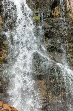 Yüksek kalitede güçlü bir şelaleye yakın çekim. Vahşi doğada güneşten sırılsıklam olmuş bir şelalenin yan görüntüsü. Dağdan büyük bir su akıntısı akıyor..