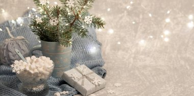 Fincanda köknar dalları, Xmas ışıkları, DIY hediye kutusu, marşmelov, örülmüş gri ekose üzerinde kar taneleri olan Xmas kompozisyonu. Sıcak, sade, sade, Danimarka kızlık zarı konsepti. Seçici odaklanma. Boşluğu kopyala.