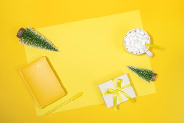 Noel çalışma alanı arkaplanı. Sarı not defteri, 2021 yılının organizatörü, küçük Xmas ağaçları, şekerli bir fincan kahve, sarı üzerine DIY hediye kutusu. Özetlemek, planlamak. Üst görünüm, düz görünüm, kopyalama alanı.