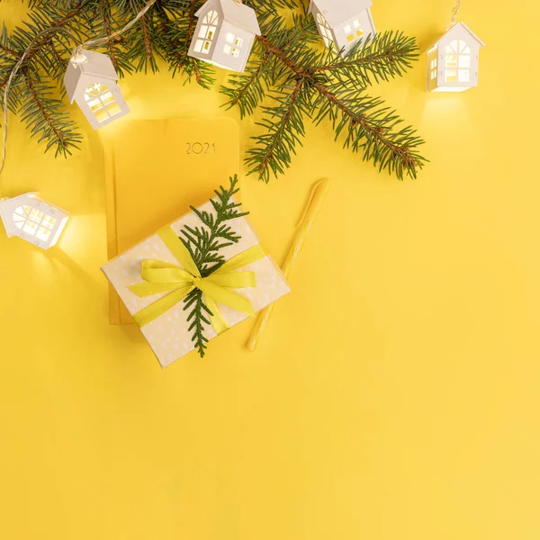 Tarjeta de felicitación de Navidad. Bloc de notas amarillo en 2021, ramas de abeto, luces de Navidad logias blancas, caja de regalo en amarillo. — Foto de Stock